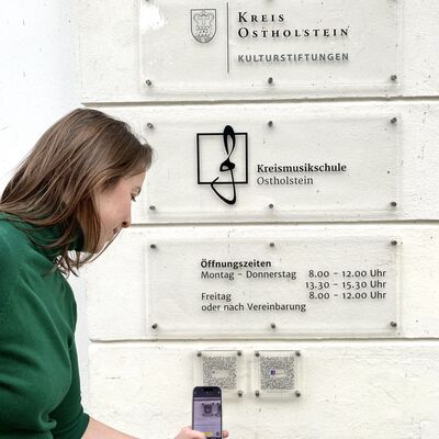 Foto einer jungen Frau, die den QR-Code der Kulturstiftung mit ihrem Handy scannt 